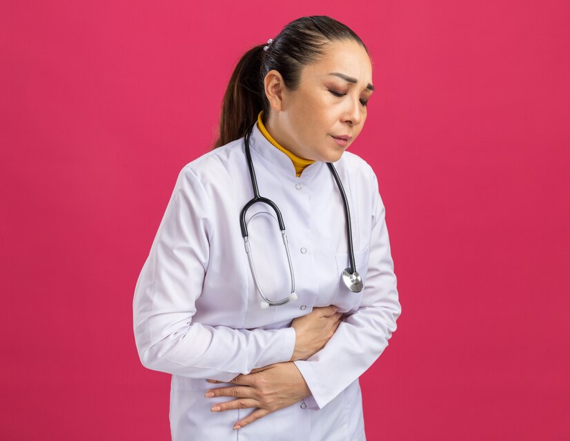 young-woman-doctor-white-medicine-coat-with-stethoscope-around-neck-touching-her-belly-looking-unwell-feeling-pain-standing-pink-wall_